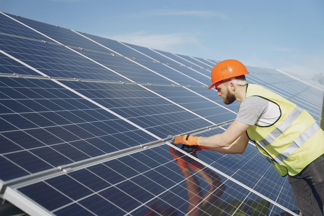 Side view of focused young man in uniform and hardhat checking setup of solar panels